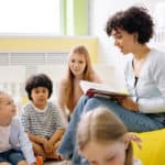 Docente leyendo un cuento a niños en aula de kindergarten fomentando la escucha y la comprensión lectora