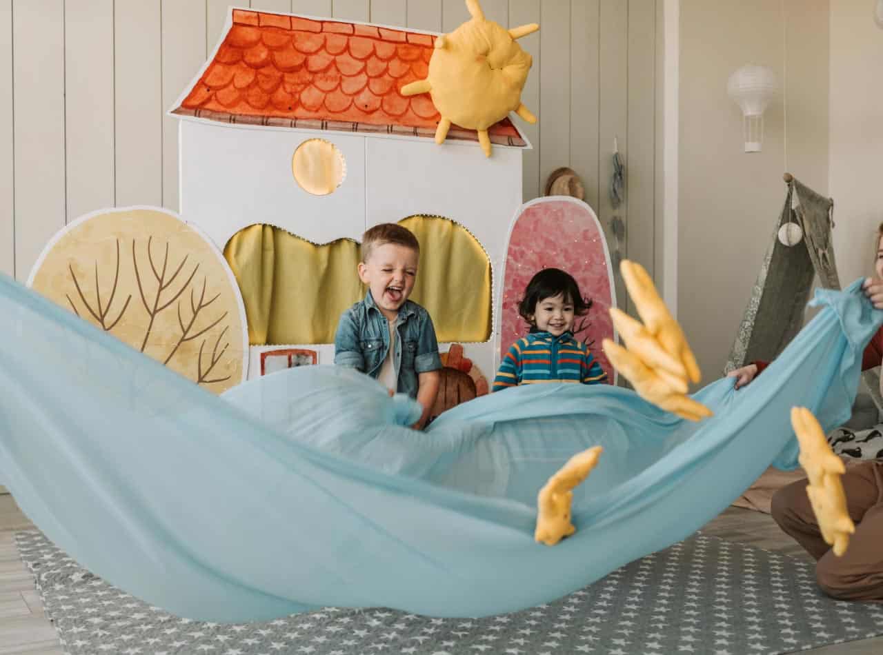 Niños en etapa Toddler participando en juego simbólico y sensorial con telas y elementos suaves en un espacio educativo
