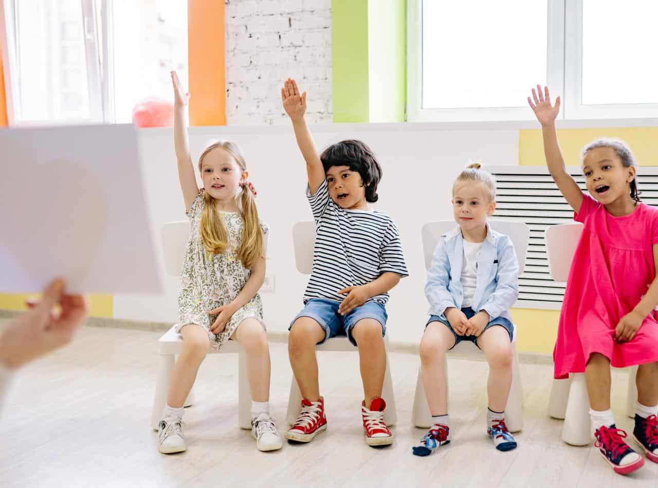 Niños en etapa Toddler levantando la mano durante una actividad educativa en el aula