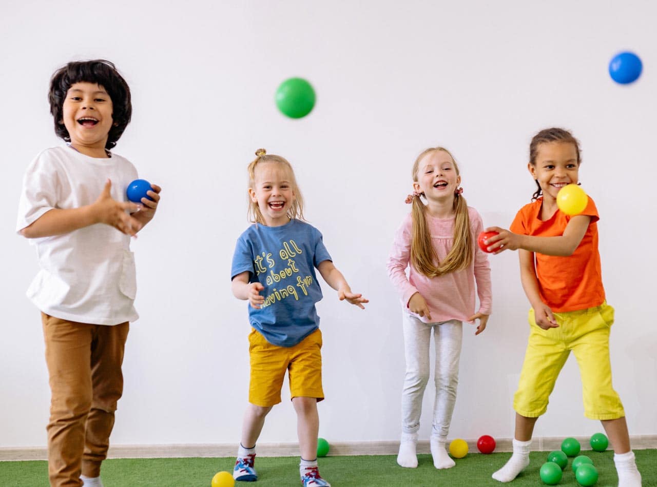 Niños Toddler jugando con pelotas de colores mientras desarrollan habilidades motrices y sociales