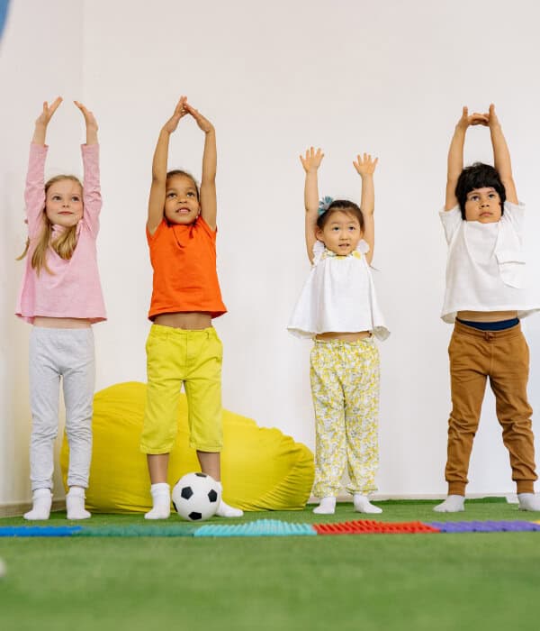 Niños realizando una actividad motriz con los brazos levantados, fortaleciendo la coordinación, el equilibrio y el movimiento corporal