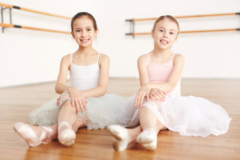 Niñas sentadas en un salón de danza infantil con vestuario de ballet, sonriendo después de una clase