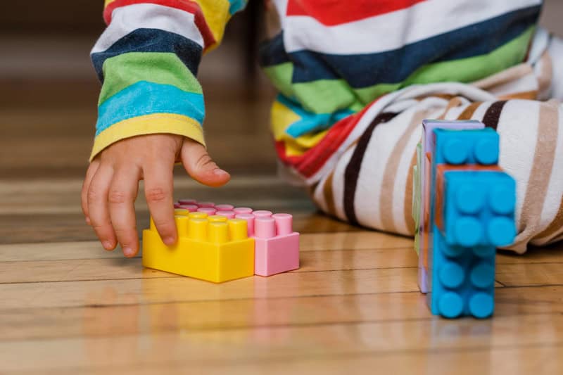 Manos de un niño jugando con bloques de construcción de colores sobre el suelo
