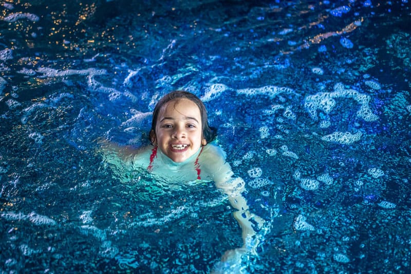 Niña sonriendo mientras nada de forma segura en una piscina