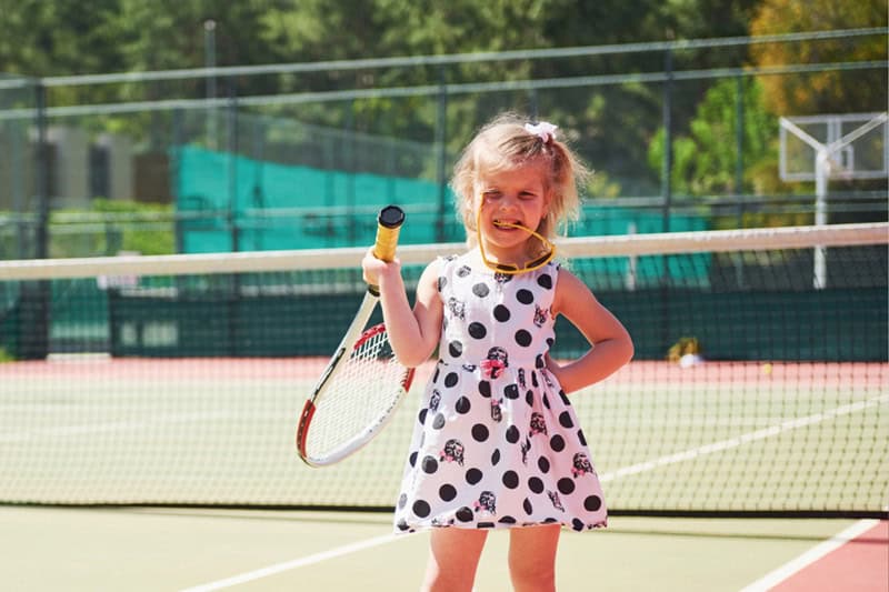Niña pequeña practicando tenis en cancha, desarrollando coordinación, equilibrio y confianza