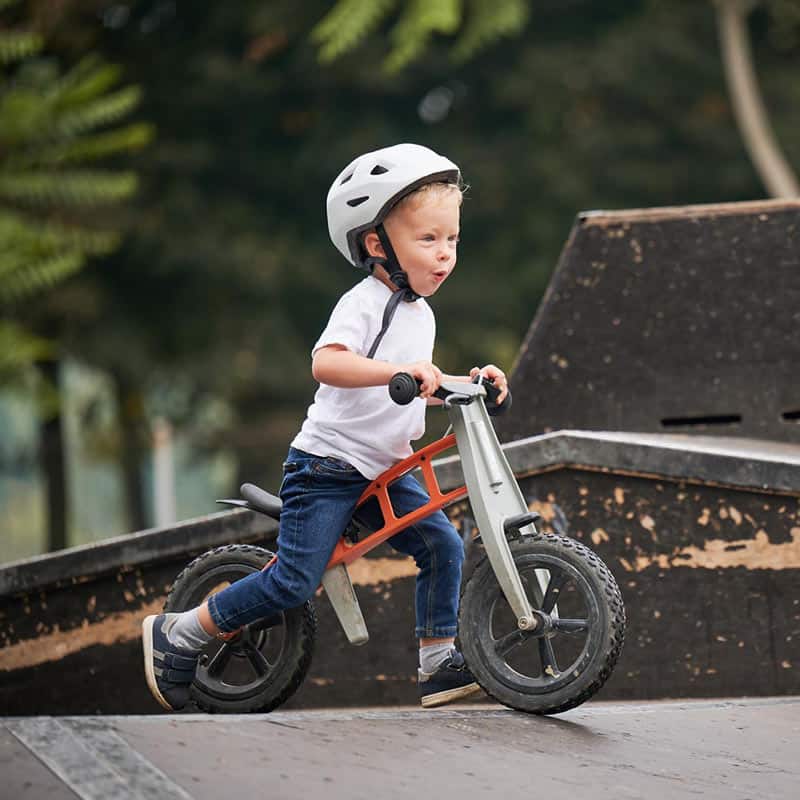 Niño pequeño en bicicleta con casco en parque infantil, educación temprana y diversión segura en Pequeños Encantos.