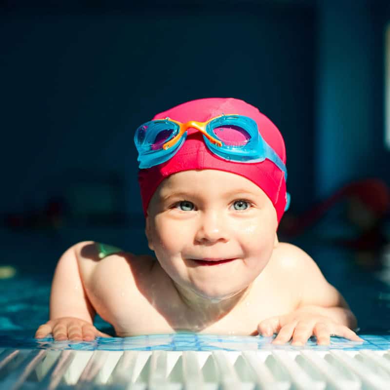 Niño en piscina con gorro y gafas de natación, disfrutando en la guardería Pequenos Encantos.