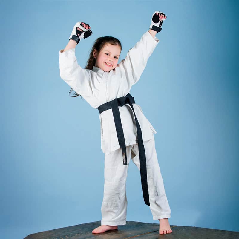 Niña en uniforme de karate levantando los brazos con entusiasmo.