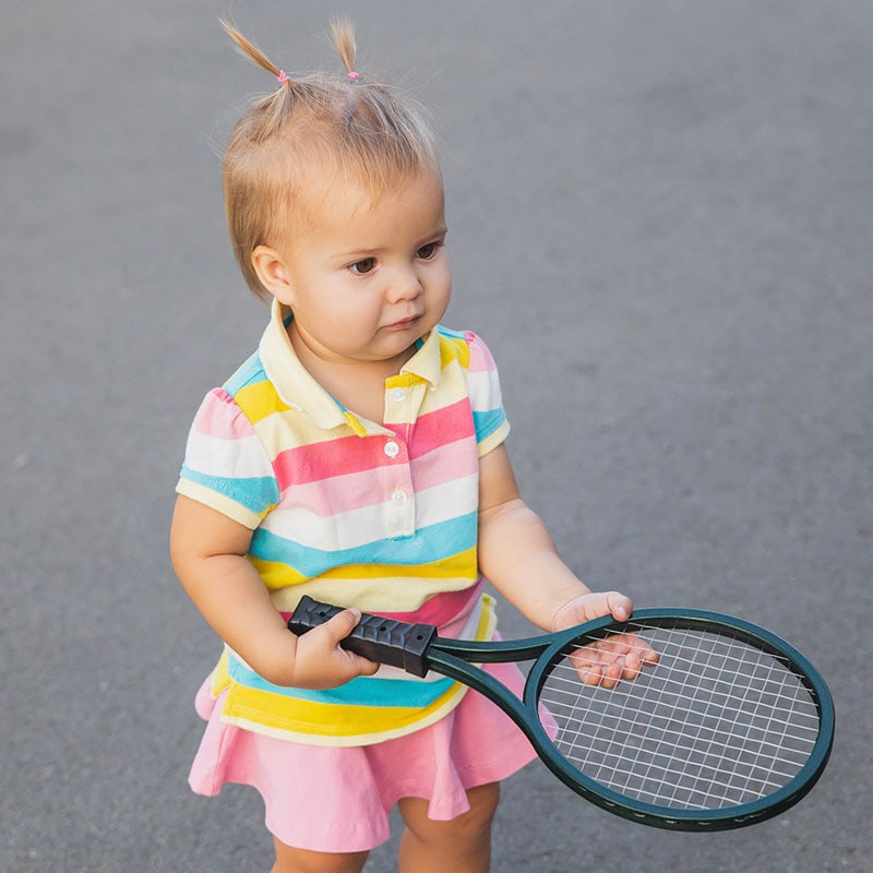 Texto alternativo: Niña en jardín infantil Pequeños Encantos con raqueta de tenis de mesa en un día soleado.